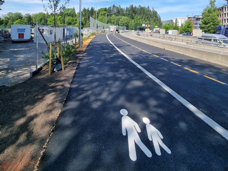 Bilde av nyasfaltert sykkelveg med fortau. Sykkelvegen har gulstripe, og på fortauet er det malt et hvitt fotgjengersymbol på asfalten av et barn og en voksen .