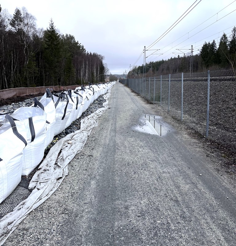 Grusvei, nettinggjerde, store plastsekker med stein, gråvær.