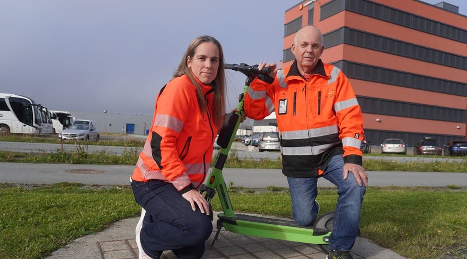 To ansatte i Statens vegvesen med en el-sparkesykkel mellom seg med Statens vegvesens bygg i Bodø i bakgrunnen.