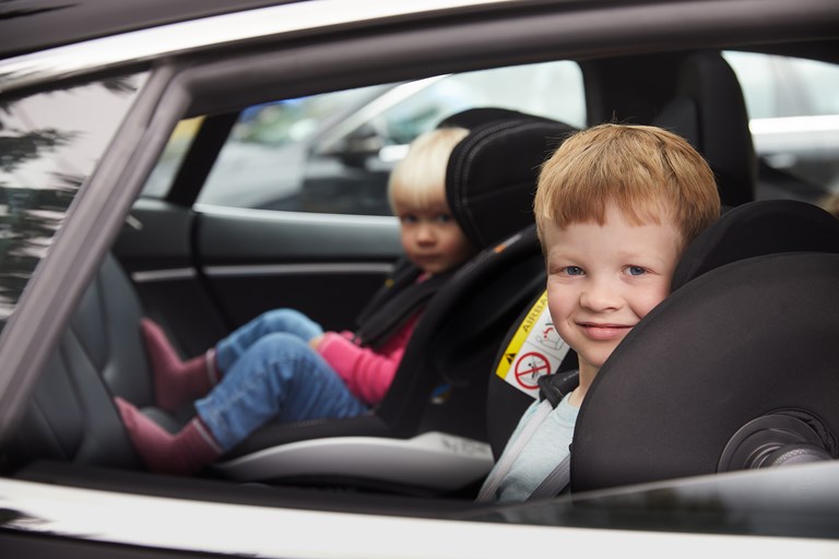 Bildet viser to barn med sikkerhetsbelte på i hver sin bilstol. 