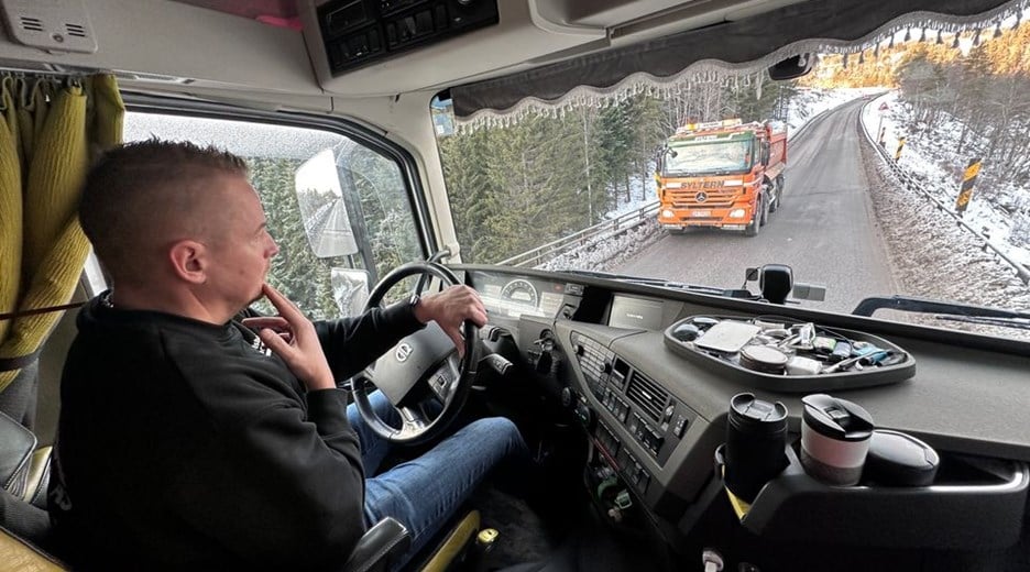 Bildet viser lastebileier Arild Olsbakk, sittende bak rattet på sin lastebil, mens han kjører på en smal veg langs dagens rv. 3. 