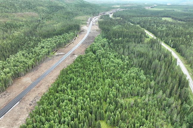 Bildet viser et dronefoto hvor vi ser en del av en strekning på den nye E6, gjennom skogen i naturskjønne omgivelser. Ved siden av den nye E6 ser vi også en del av den gamle E6 som nå skal gjøres om til driftsveg for skogbruket. 