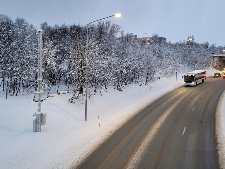 Foto av E8 Tverrforbindelsen i Tromsø: Den nye værstasjonen (til venstre) har en rekke sensorer som gir verdifulle data om temperatur, nedbør og friksjon til entreprenørene som drifter vegen.