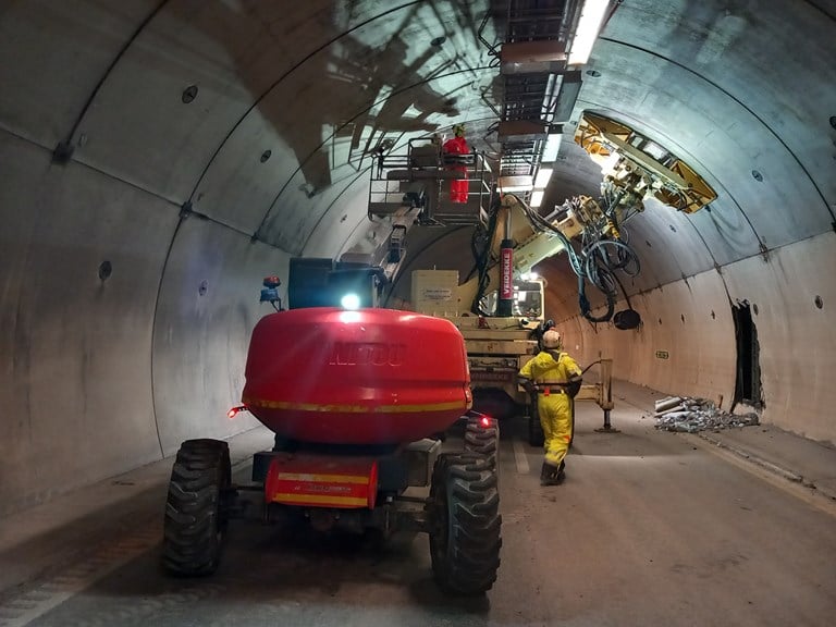 Store maskiner inne i en tunnel og et hull i tunnelveggen i bakgrunnen.