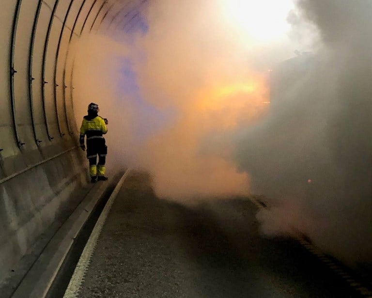 Mye røyk inne i en tunnel. En person i vernetøy står i røyken.